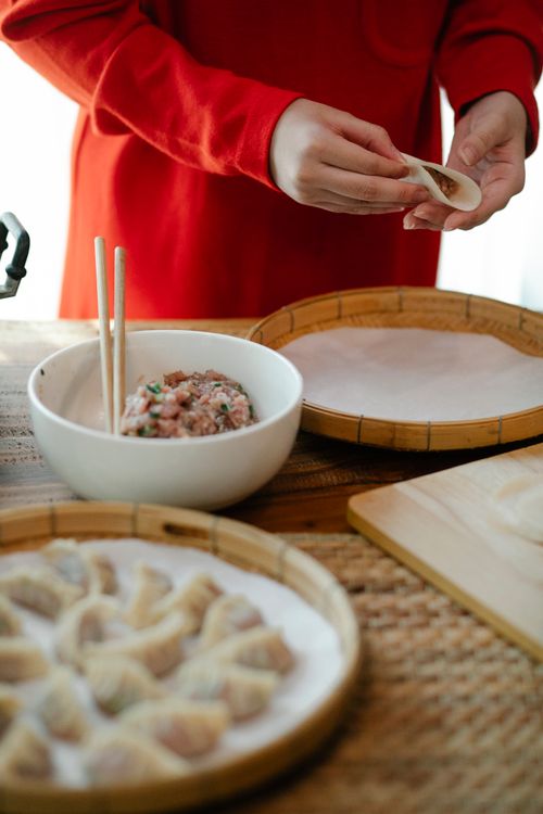 Free Crop unrecognizable female preparing dumplings with ground meat filling at table with bamboo trays in house Stock Photo