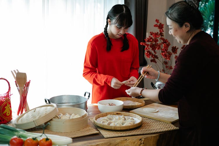 Smiling Asian Grandmother With Granddaughter Filling Dim Sum In Kitchen