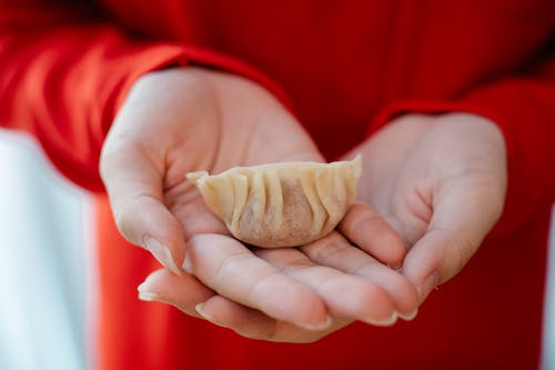 Crop unrecognizable person in red clothes showing homemade jiaozi dumpling in hands in daylight