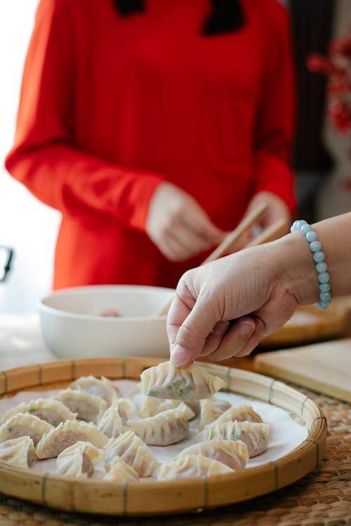Crop anonymous women preparing traditional Chinese jiaozi dumplings while standing at table in kitchen in daylight