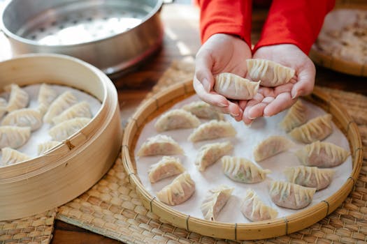 From above of crop anonymous female chef demonstrating traditional raw Asian dumplings before serving on tray in kitchen
