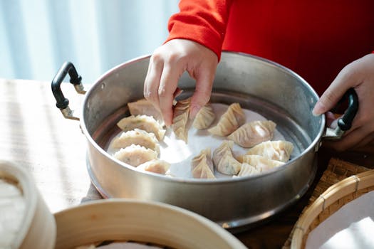 Hands arranging fresh dumplings in a steamer, showcasing traditional homemade cooking indoors.
