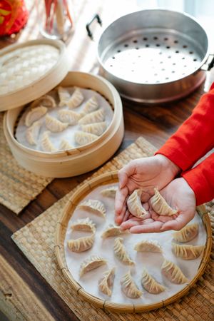 Hands folding dumplings with pleated edges