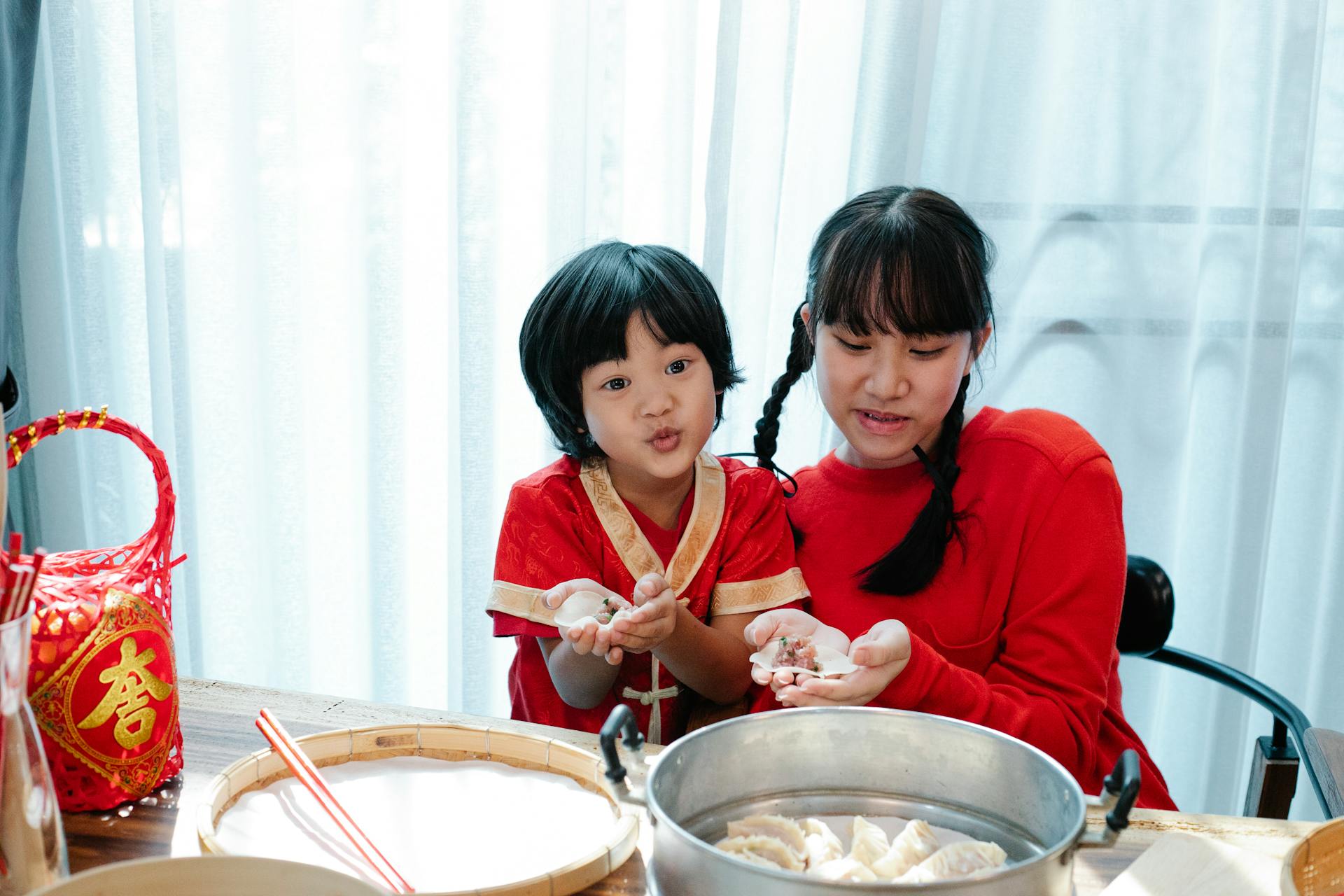 High angle of cute ethnic boy cooking traditional Asian jiaozi at table with sister in kitchen