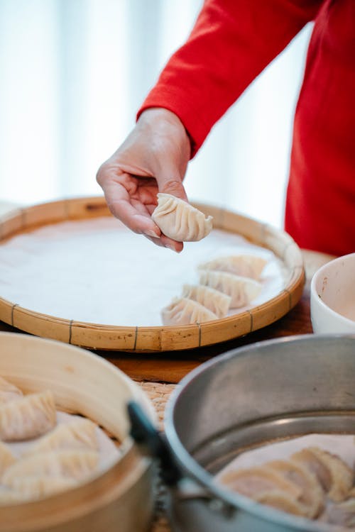 Free From above of crop anonymous female cooking homemade dumplings in bamboo steamer in kitchen Stock Photo