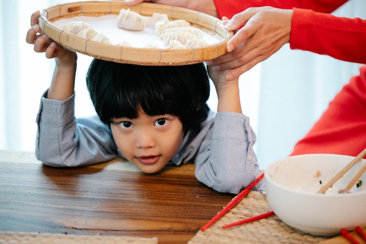 Funny Ethnic Kid With Bamboo Tray Of Dumplings On Head