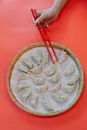 Top view of crop anonymous female with bamboo chopsticks taking uncooked homemade jiaozi on red background