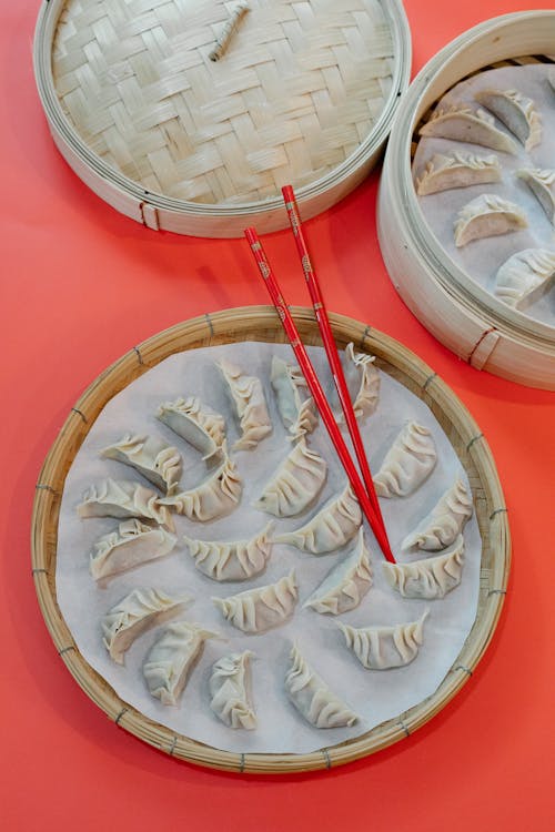 From above of uncooked dumplings on bamboo trays for boiling with chopsticks on red table