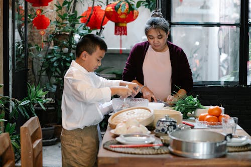 Free Focused ethnic boy mixing ingredients for stuffing for cooking traditional Chinese dumplings with granny at kitchen Stock Photo