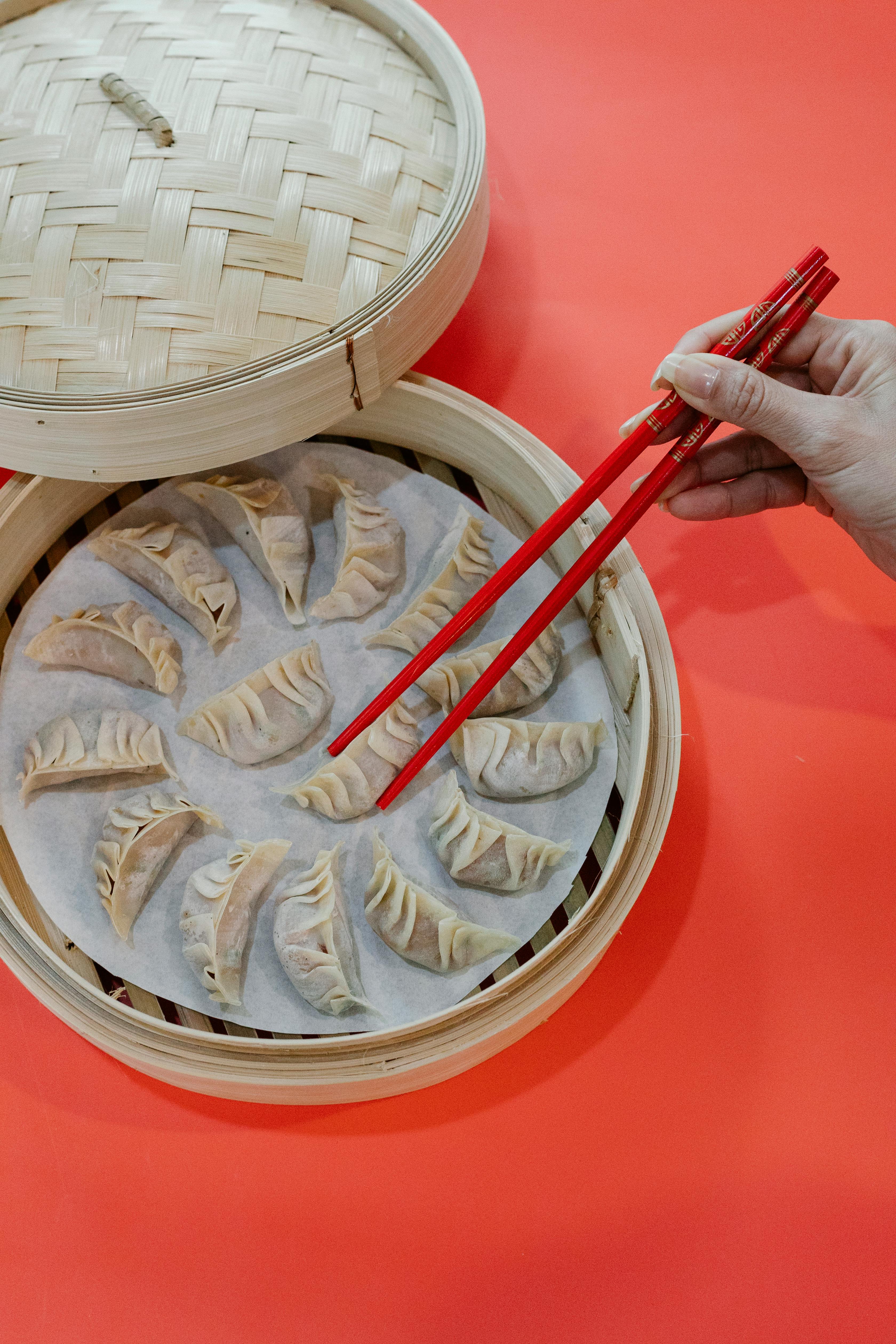 woman taking raw dumpling from bamboo steamer