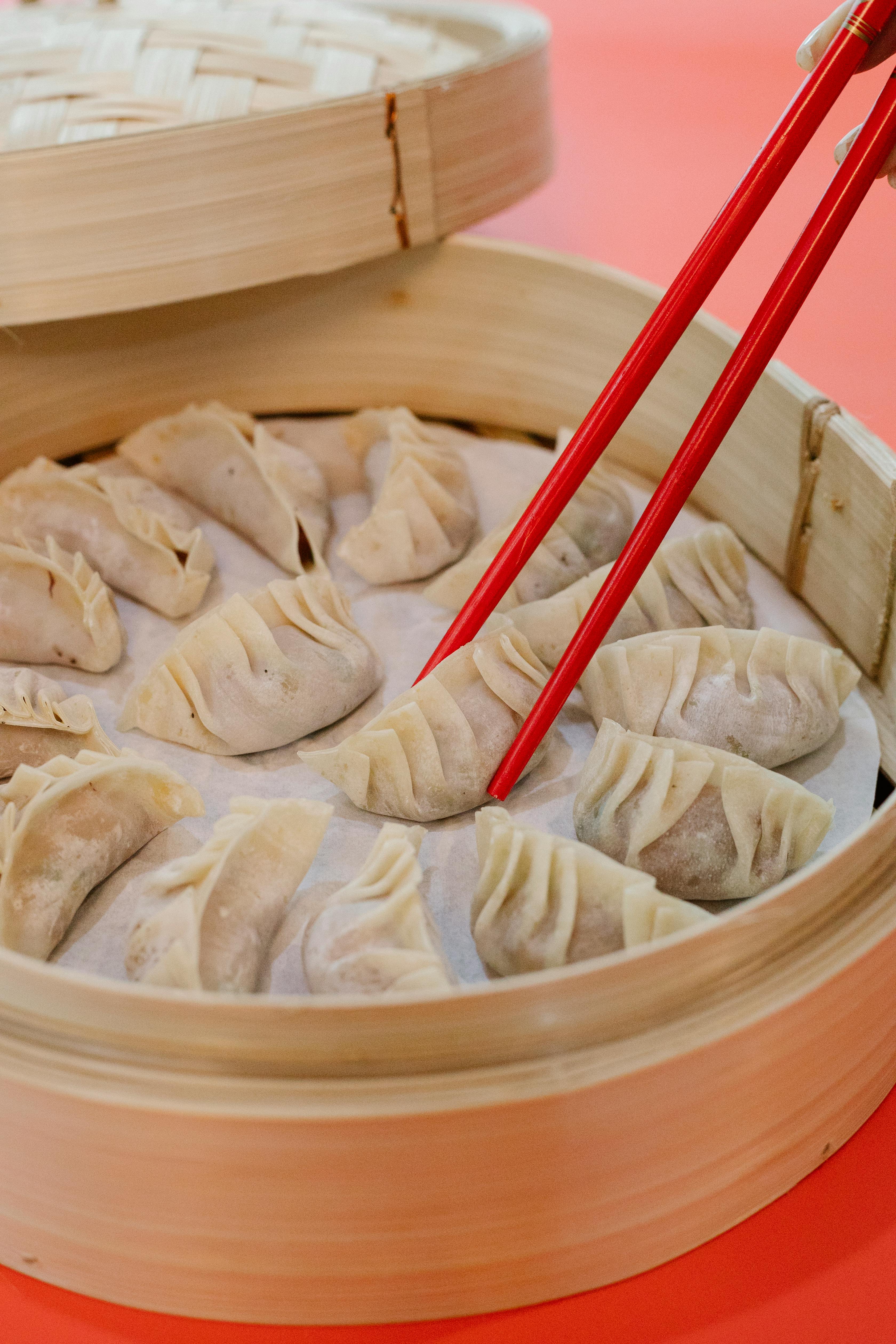 woman taking raw dumpling with bamboo chopsticks