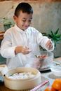Smiling ethnic boy with spoons preparing stuffing for dumplings while cooking traditional food in kitchen