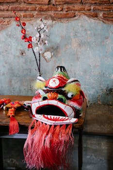 Vibrant Chinese dragon mask displayed on a wooden table with decorative cherry blossoms in the background.