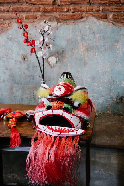 Vibrant Chinese dragon mask displayed on a wooden table with decorative cherry blossoms in the background.