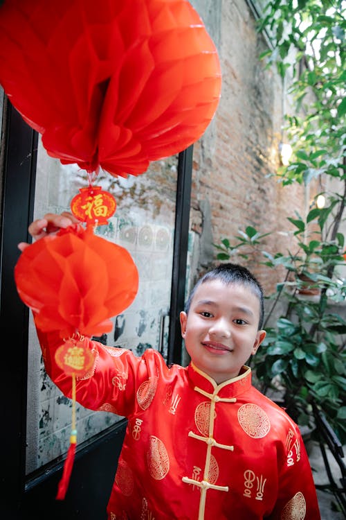 A Boy in Red Clothes Touching a Red Lantern