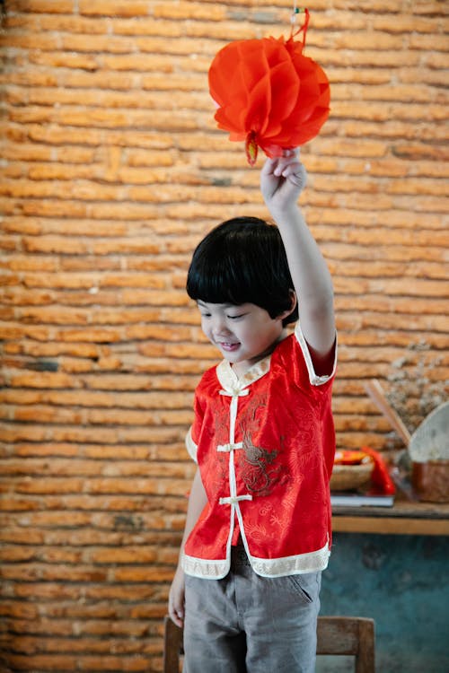 A Boy in Red Clothes Touching a Red Lantern