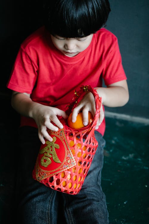 Cute ethnic boy putting tangerines into red basket