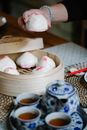 High angle of crop anonymous female taking homemade bao from bamboo steamer placed on table near tea set