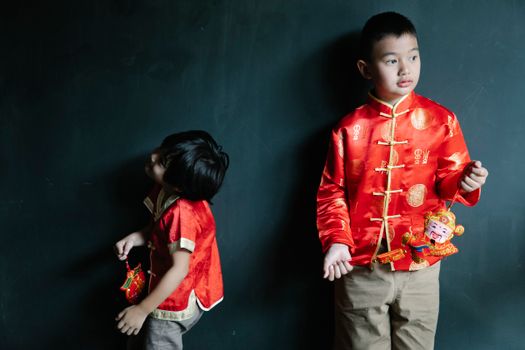 Playful Asian boy wearing traditional clothes standing near brother with decor for Chinese New Year