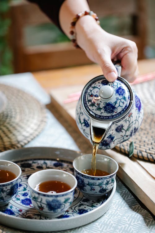 High angle of female pouring herbal tea into ceramic cups placed on tray for Chinese ceremony