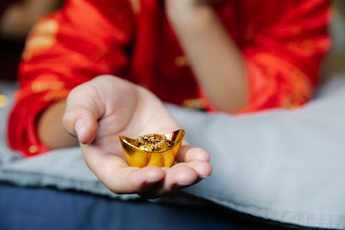 Crop anonymous person in authentic outfit showing Chinese gold bar presented for New Year