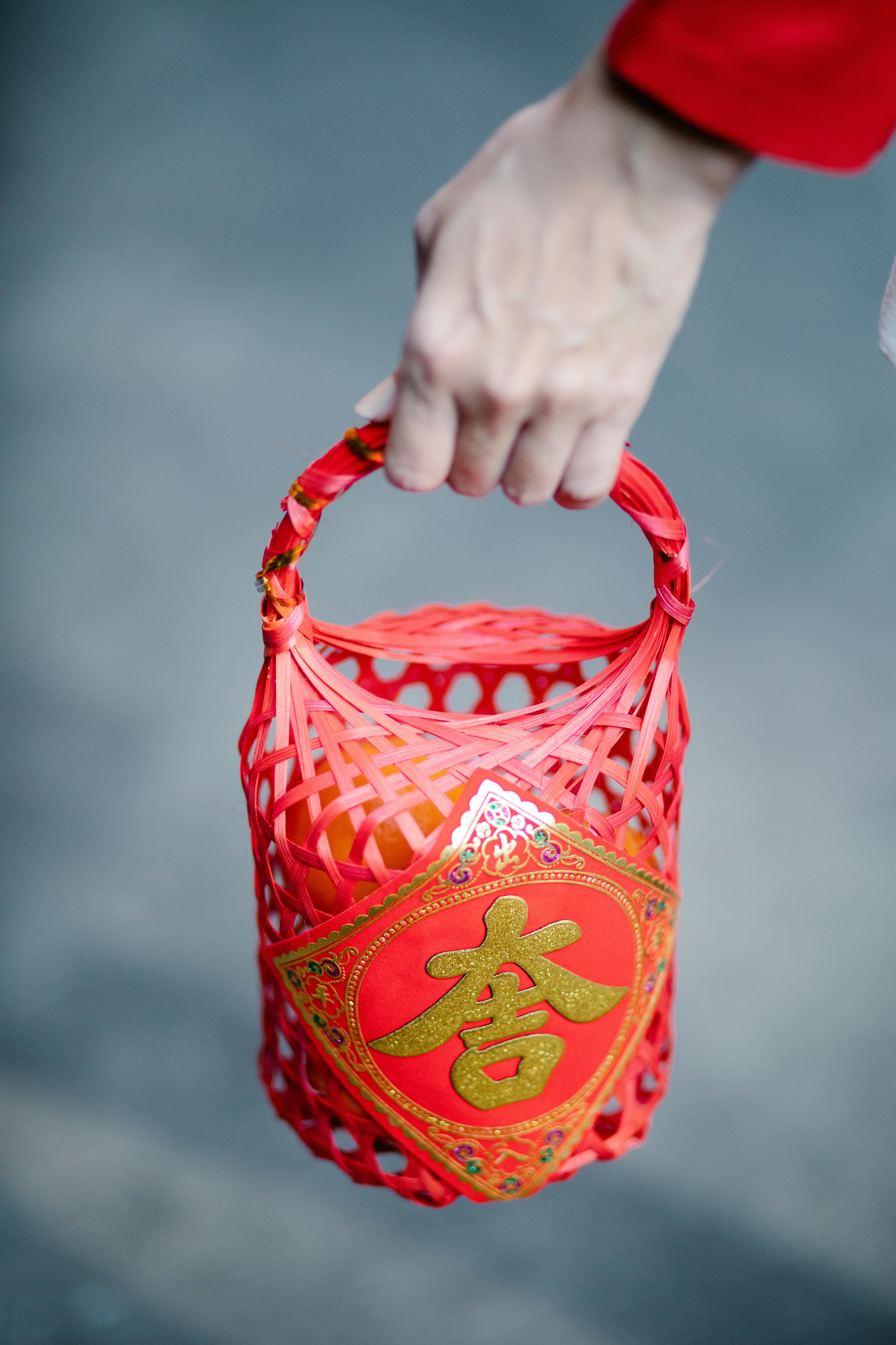 A hand holds a decorative red basket, symbolizing Chinese New Year festivities and traditions.