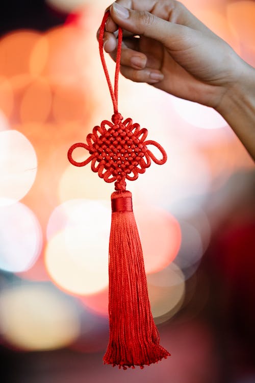 Crop anonymous female with traditional Chinese knot for New Year decor against blurred glowing lights