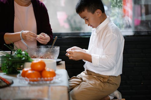 Focused ethnic boy making dumplings with grandmother