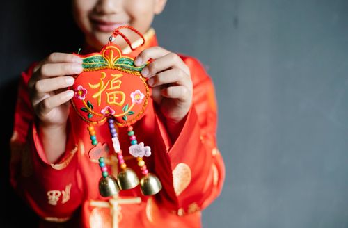 Free Crop smiling boy wearing traditional festive outfit showing decorative toy for New Year while standing near gray wall Stock Photo