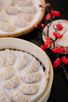 From above of homemade raw jiaozi dumpling in wooden steamer placed near blooming branch of sakura