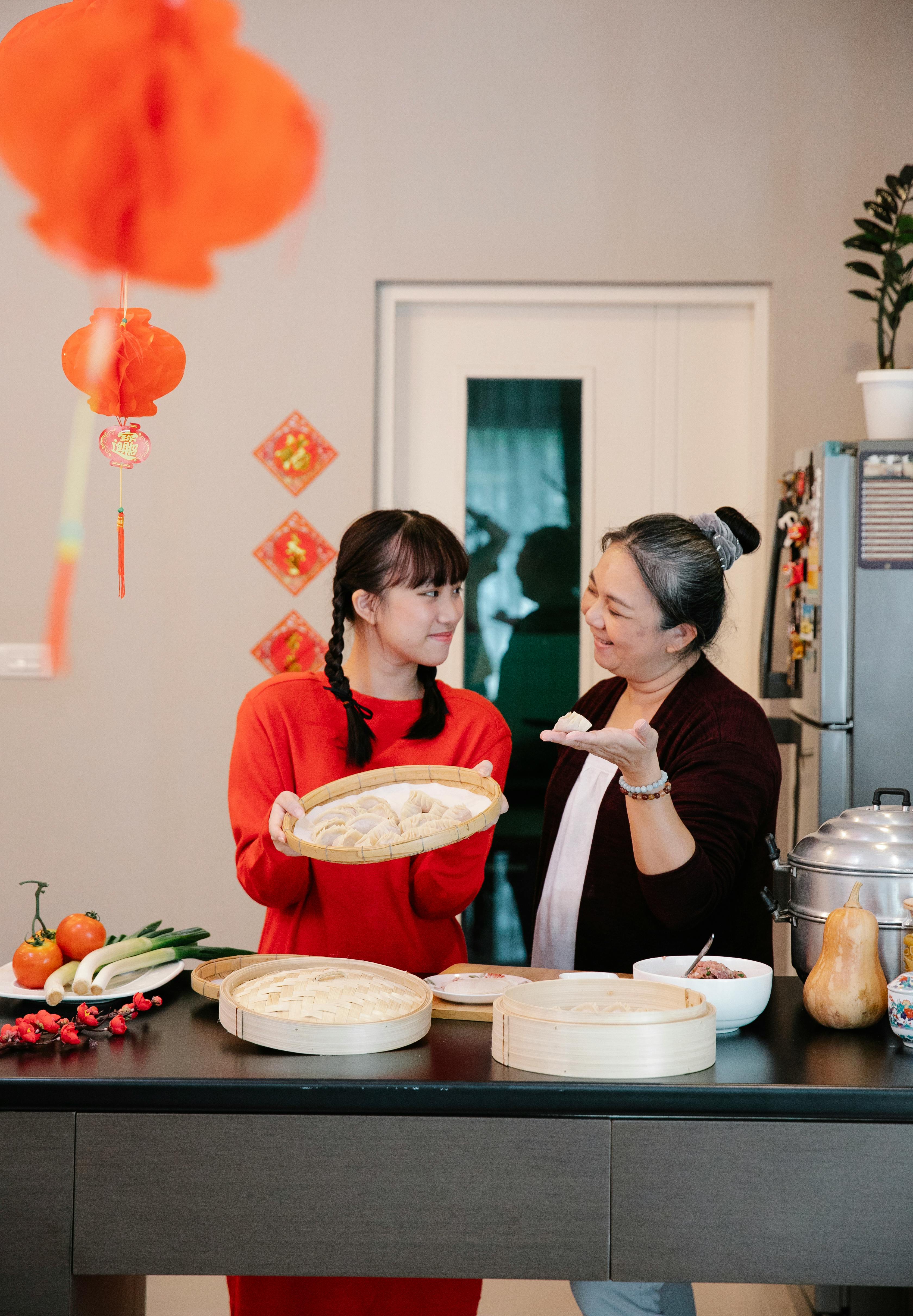 smiling asian granddaughter and grandmother showing raw dumplings