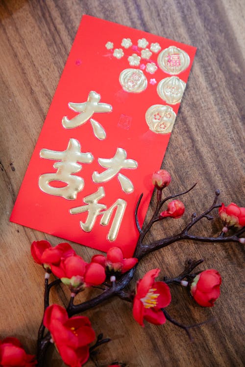 From above of traditional Chinese New Year envelope with hieroglyph placed near artificial sakura branch