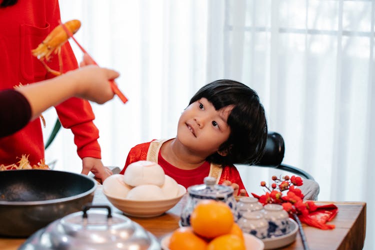 Crop Person With Cooked Prawn Against Asian Boy At Home