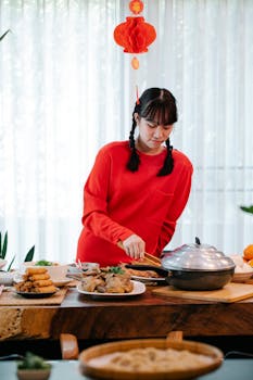 Asian teen girl in red sweater preparing a festive meal with traditional dishes indoors, celebrating a cultural holiday.