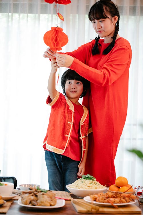 Asian teen with brother decorating home with red lantern