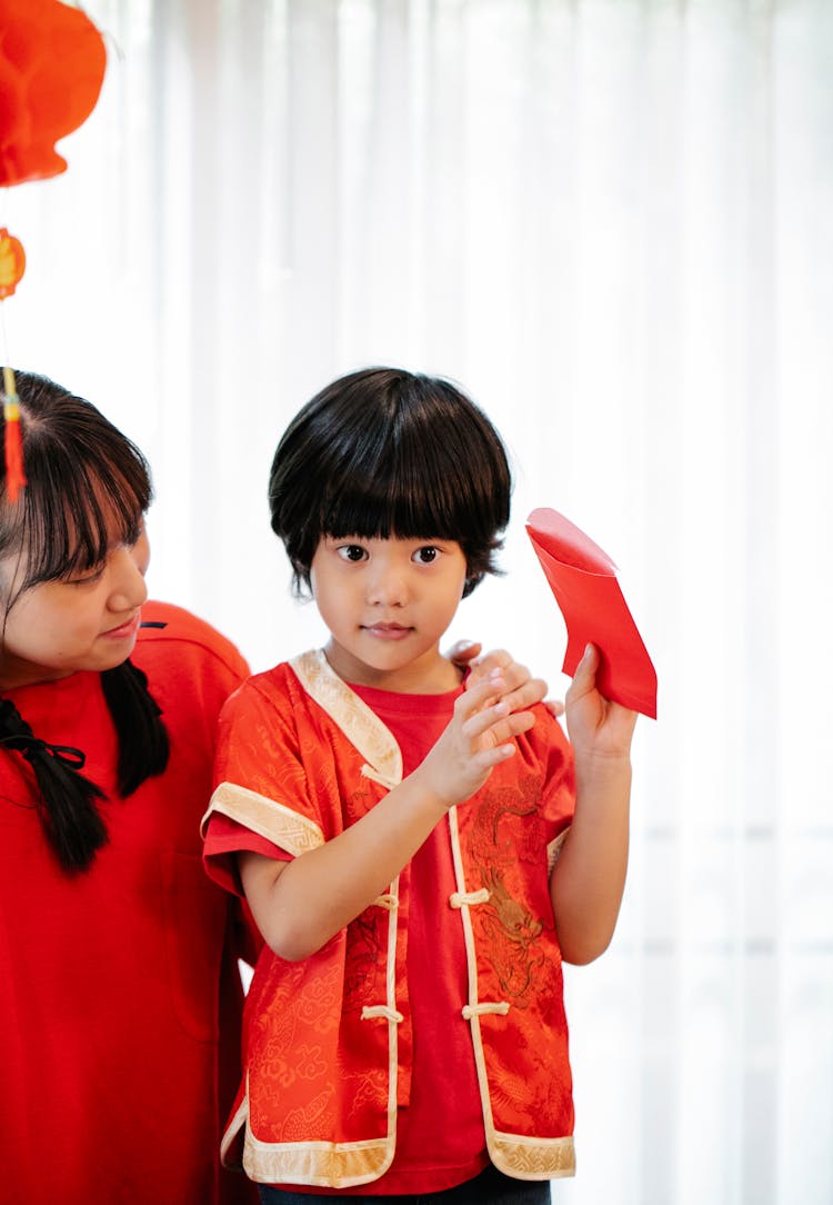 Asian Boy With Red Packet Against Crop Sister At Home