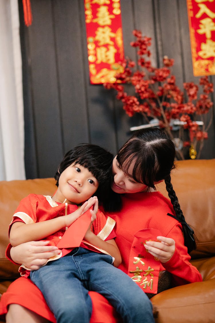 Asian Teen Embracing Brother With Red Envelope On Sofa