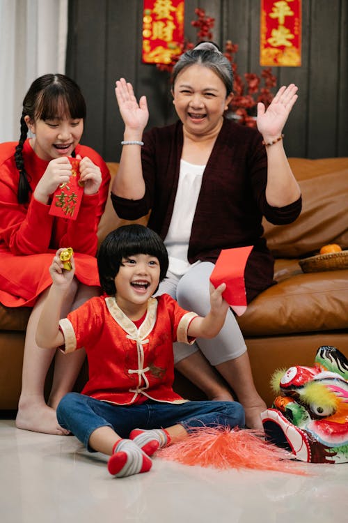 Positive ethnic grandma with granddaughter and grandson with red envelope celebrating New Year holiday in house