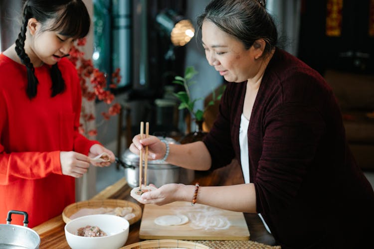 Positive Senior Ethnic Woman With Granddaughter Preparing Jiaozi In Kitchen