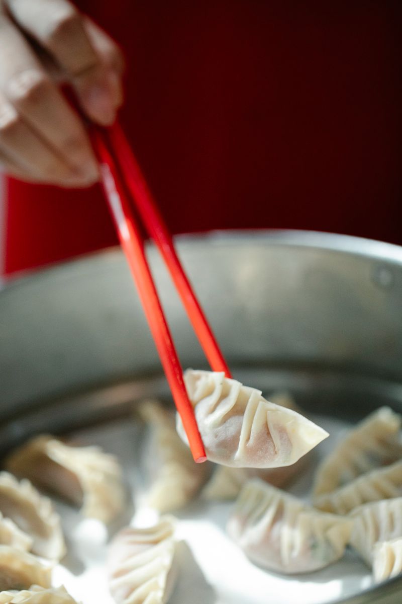 Chopsticks lifting a soup dumpling from a steamer basket