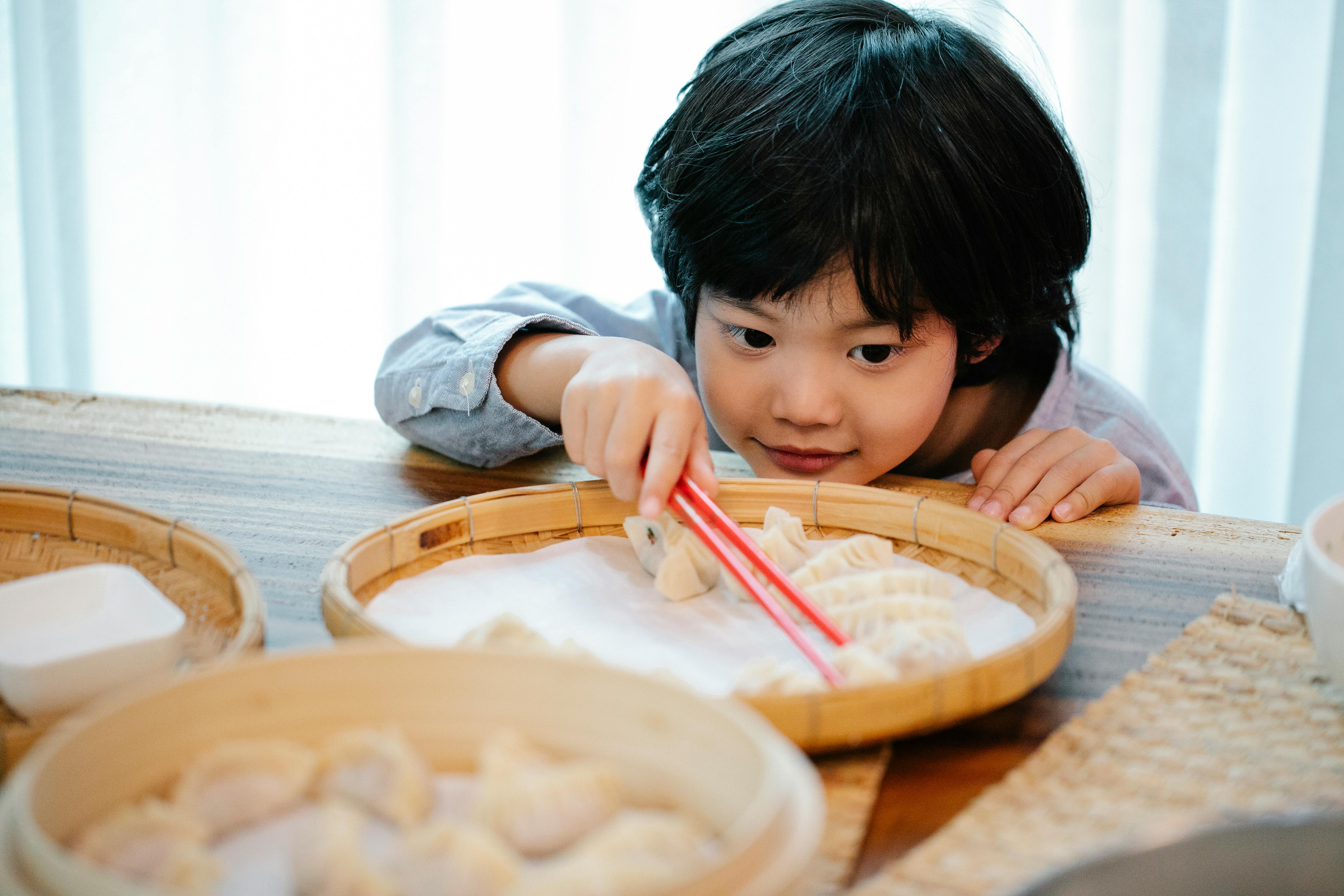 an adorable child picking up a dumpling using chopsticks