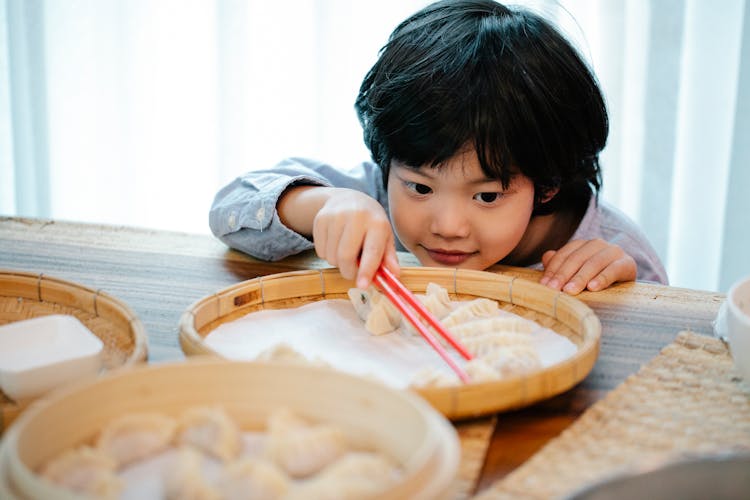 An Adorable Child Picking Up A Dumpling Using Chopsticks