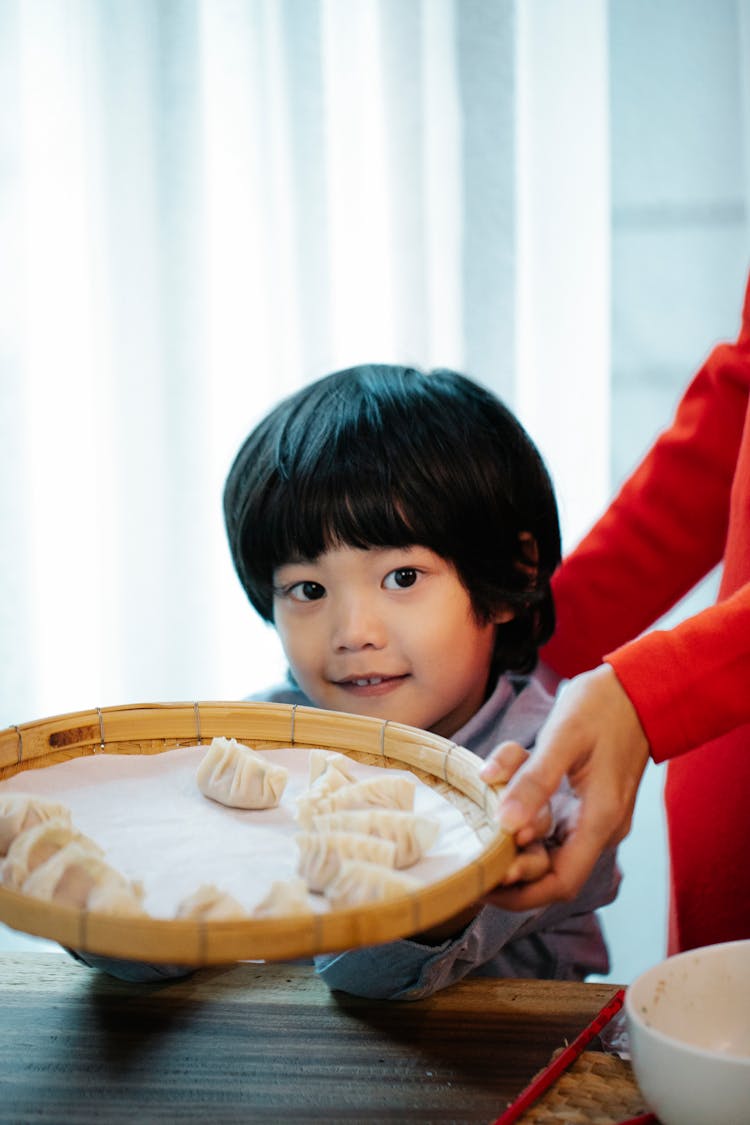 A Child Holding A Tray With Dumplings