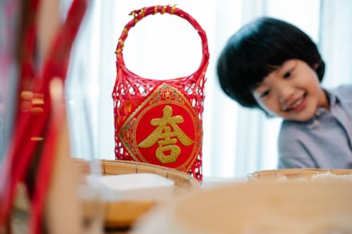 Cheerful little ethnic boy with dark hair smiling while sitting at table with Asian decorations and ingredients in kitchen