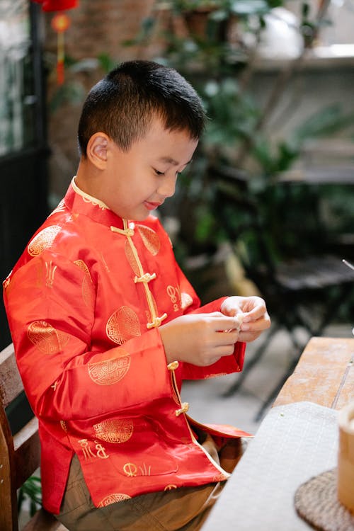 Positive ethnic boy folding Chinese dumplings at table in kitchen