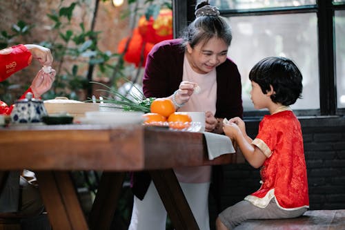 Free Smiling mature ethnic woman helping little grandson to fold Chinese dumplings Stock Photo