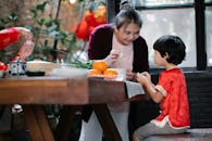 Smiling mature ethnic woman helping little grandson to fold Chinese dumplings
