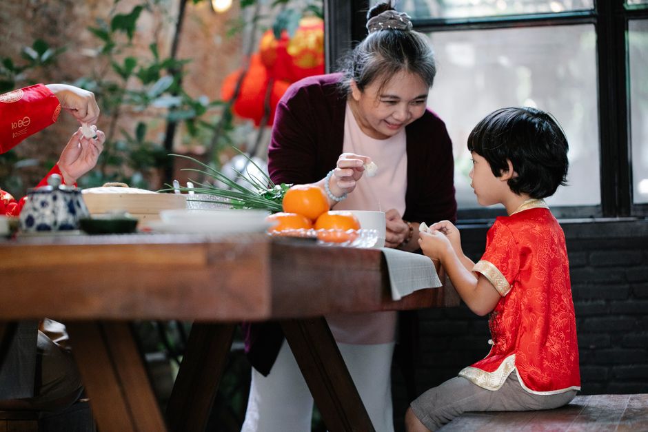 A grandmother teaching her grandson to fold dumplings in the kitchen while chatting