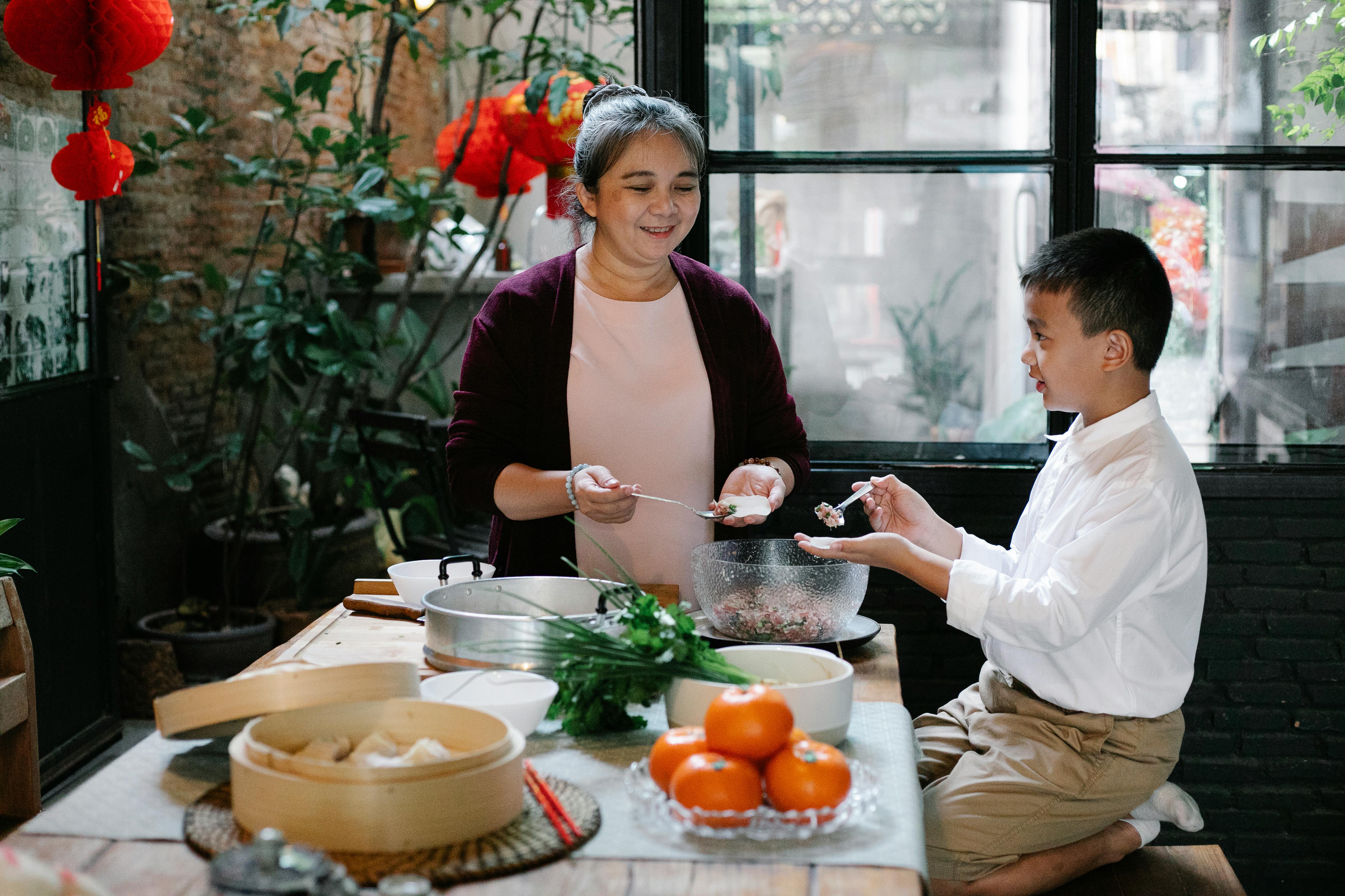 happy ethnic grandmother teaching preteen grandson to fold jiaozi