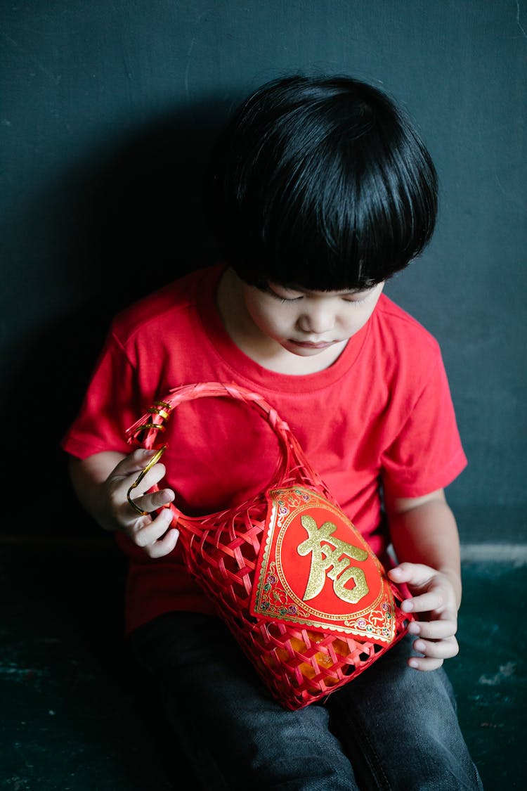 Adorable Ethnic Little Boy Holding Gift Basket Near Dark Wall